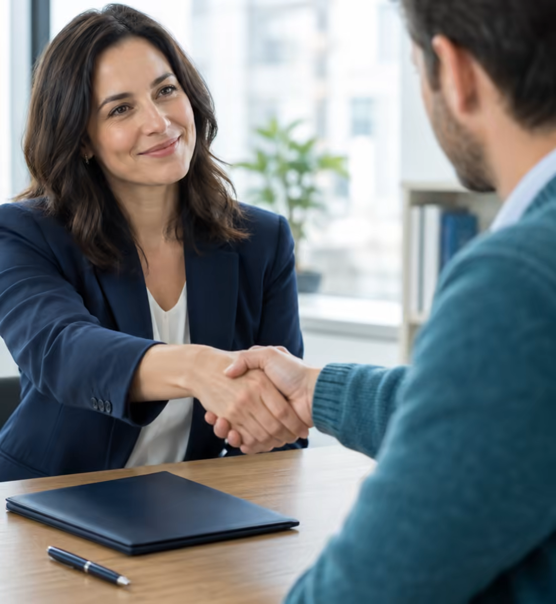 A broker and a client shaking hands across a desk